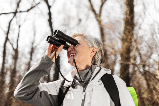 escursionista anziano maturo che guarda attraverso il binocolo - osservare gli uccelli foto e immagini stock