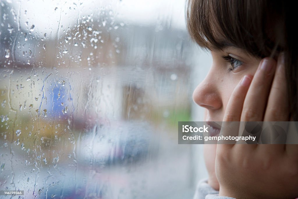 Girl looking out a rain splattered window young child looking out of window on rainy day Rain Stock Photo