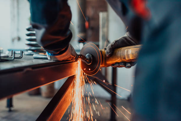 Locksmith in special clothes and goggles works in production. Metal processing with angle grinder. Sparks in metalworking.