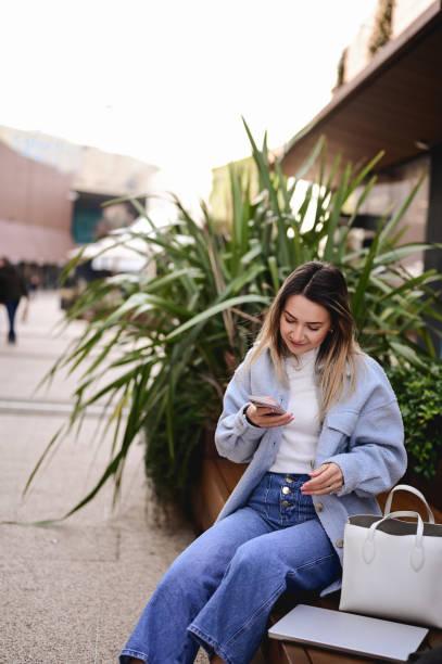 istock woman sitting outside on bench reading a text message on telephone. 1467423663