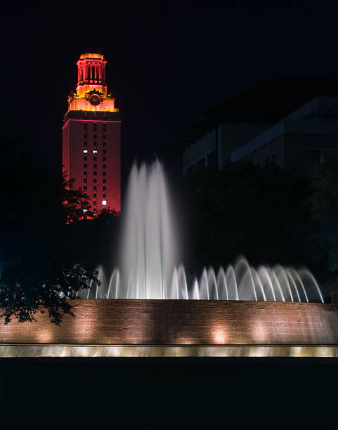 UT Tower - University of Texas at Austin Night image of the University of Texas at Austin (UT) clock tower, part of the main building, lit orange in celebration of a Longhorn victory, behind the beautiful East Mall fountain. clock tower stock pictures, royalty-free photos & images