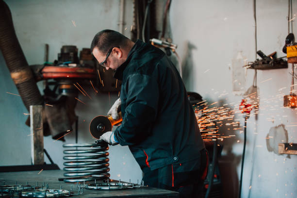 istock Locksmith in special clothes and goggles works in production. Metal processing with angle grinder. Sparks in metalworking. 1467424403