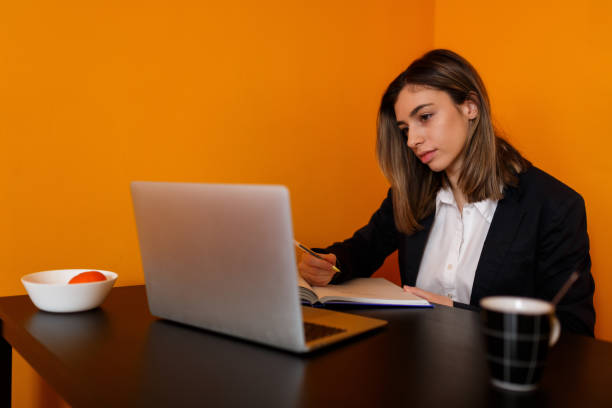 istock Woman Sitting At Desk Using Laptop, Writing in Notebook 1467426621