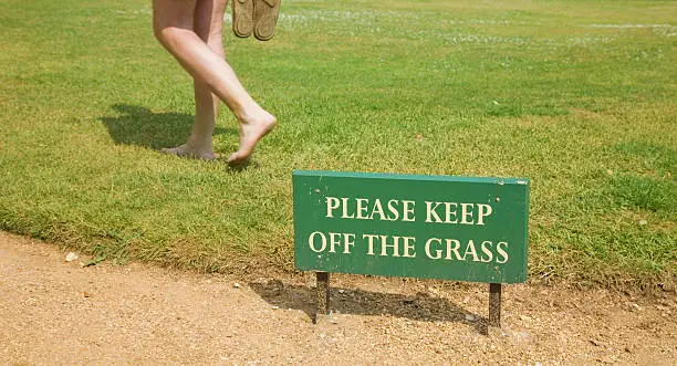 rulebreaker (man walking on a grass behind "keep off" sign)