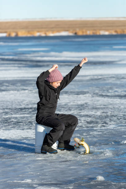 Young girl who has just caught a walleye while ice fishing on a beautiful winter day. In this image the fish is just coming up through the hole in the ice.