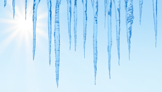 Close-up of icicles on a blue sky with shining sun background.