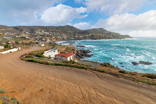 The rocky, scenic coastline and small town with waterfront buildings along the Pacific Ocean at the cape of Punta Banda, southwest of the city of Ensenada, Mexico near La Bufadora Blowhole.