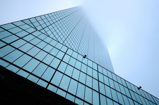 Low angle view of modern skyscraper disappearing in the fog. Abstract composition ideal for business concept or background.