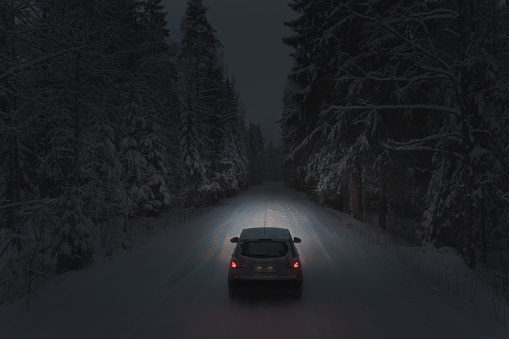 Car on a snowy forest road at night. Back view. Themes of road transport and travel
