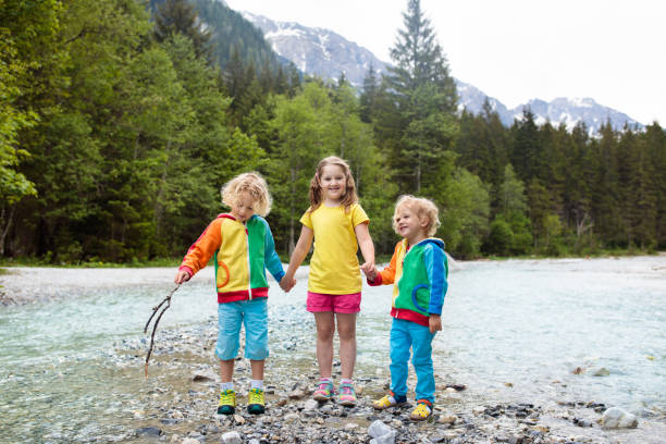 Children hiking in Alps mountains crossing river. Kids play in water at mountain in Austria. Spring family vacation. Little boy and girl on hike trail. Outdoor fun. Active recreation with children.