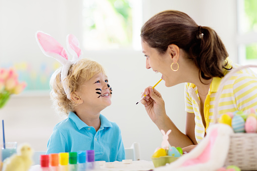 Mother and kids color Easter eggs. Face painting for little child. Little boy with bunny ears and mom dye eggs. Easter egg hunt. Family celebration and home decoration for spring holiday.