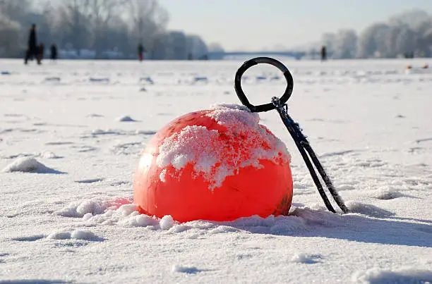 A small red buoy is icebound in a lake