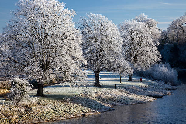 two sledgers enjoy the pristine snow conditions in a field in Buckinghamshire on a winter's afternoon. Oak trees covered in frost and snow sit on the hillside whilst the late sun is breaking through the clouds in the background.