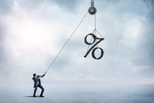 A man uses a rope and puley to raise a large percentage sign.