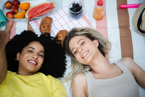 Portrait of two happy best female friends lying down on a rug and enjoying a picnic together