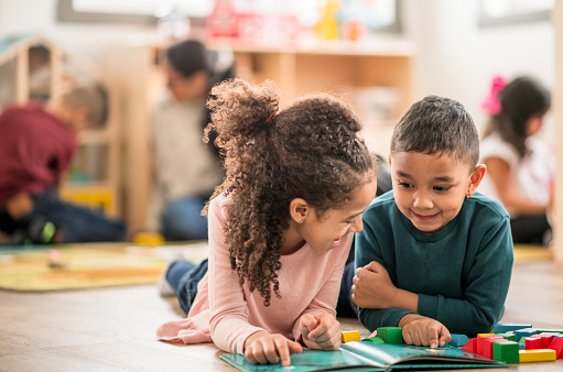 Two kids laugh while they read and play together in the daycare classroom.