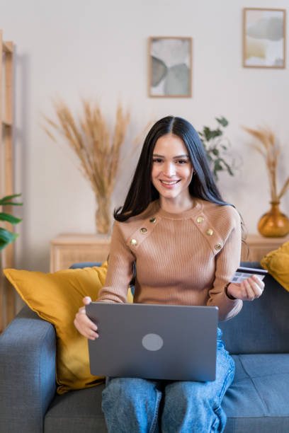 istock Smiling woman using laptop on sofa shopping online 1467462650