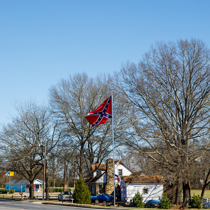 Hickory, NC, USA-18 Feb 2023: Older rock home with large confederate flag on tall flag pole.  Sunny, blue sky day.  Square image.