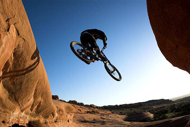 Jumping off in Moab A mountain biker takes to the air in the early morning. mountain bike stock pictures, royalty-free photos & images