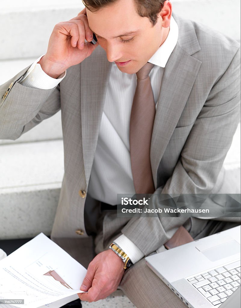 Uomo d'affari parlando sul cellulare con laptop e documenti accanto a lui - Foto stock royalty-free di 20-24 anni