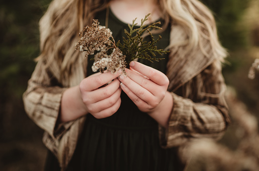 Child holding pine needle branch and dried flowers