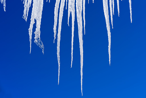 Icicles Hanging From Roof Against Blue Sky - Crisp large ice hanging from roof eaves.