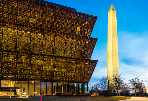 Washington D.C., USA - February 10, 2023: The National Museum of African American History and Culture at night with the Washington Monument in downtown Washington DC.