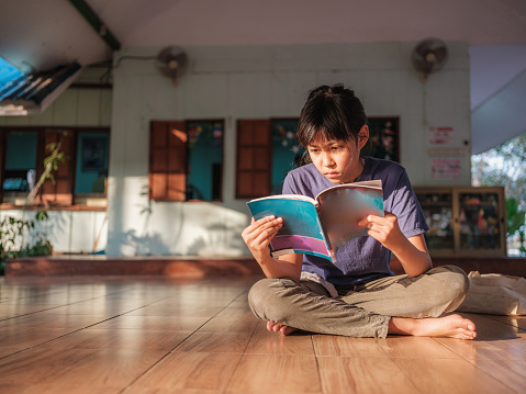 Portrait of young Asian girl reading a book while sitting on the ground at terrace home, Education and knowledge concept