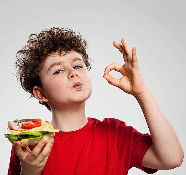 Boy eating sandwich showing OK sign
