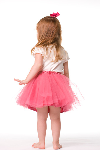 From behind, a little red-haired ballerina wearing a pink tutu. 