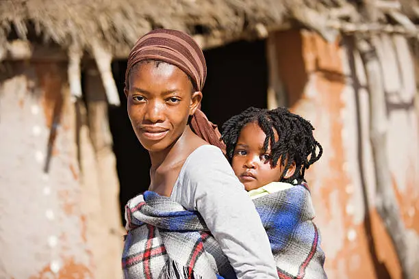 African mother carry child in a traditional way in front of the hut