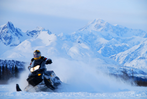A snowmobile races away from Alaska's Mt. McKinley in a blur of speed with snow whirling in the background during a winter, evening ride.
