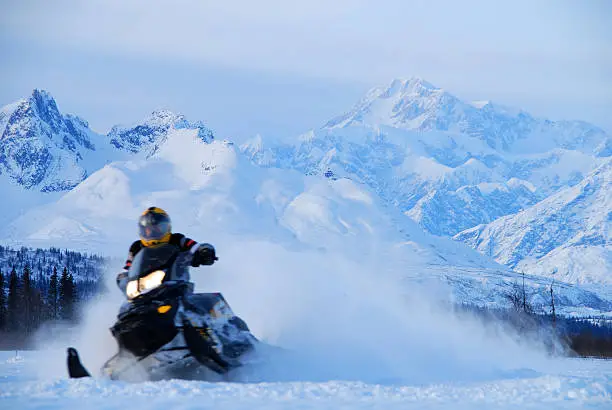 A snowmobile races away from Alaska's Mt. McKinley in a blur of speed with snow whirling in the background during a winter, evening ride.