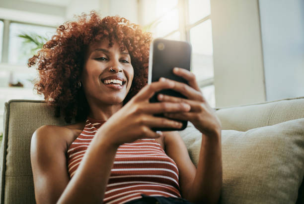 mulher feliz, telefone e comunicação no sofá de casa para bate-papo aplicativo móvel de mídia social. pessoa com smartphone digitando e-mail, postagem de blog e pesquisa ou lendo meme engraçado na internet com wifi para relaxar - relaxation working humor sofa - fotografias e filmes do acervo