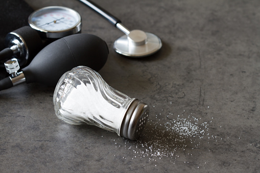 Salt shaker and blood pressure monitor, high salt content in diet and hypertension concept background
