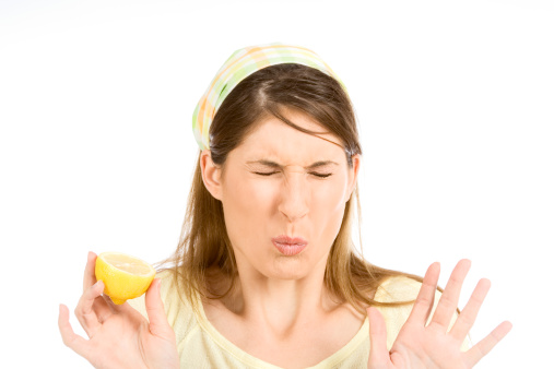 Female makes a very sour grimacing face eating fresh lemon