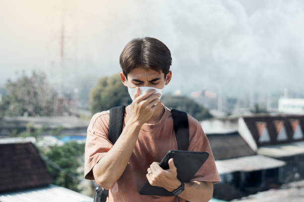 Portrait Asian young man wear N95 mask to protect PM 2.5 dust and air pollution. Young man wearing protection mask over smog city building with bad weather, pm2.5,City air pollution concept. retrato joven asiático usa máscara n95 para proteger el polvo pm 2.5 y la contaminación del aire. joven con máscara de protección sobre el edificio de la ciudad de smog con mal tiempo, pm2.5, concepto de contaminación del aire de la ciudad.