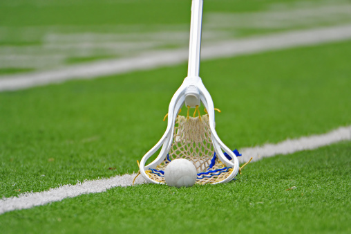 Mens lacrosse stick scooping up the ball on a turf field.