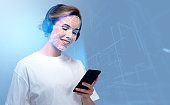 Smiling businesswoman wearing headphones typing on smartphone with facial recognition