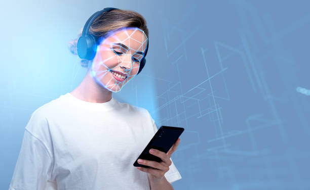 Smiling businesswoman wearing headphones typing on smartphone with facial recognition stock photo