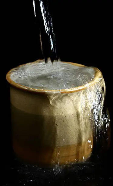 Cup of water that is overflowing, isolated on black background.