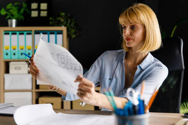 istock Focused businesswoman analyzing blueprint documents at desk 1467573070