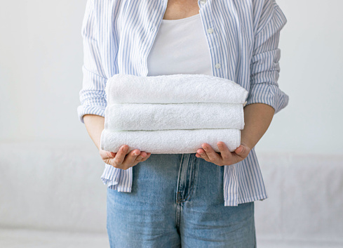 A woman holds a stack of clean, neatly folded white towels in her hands. The concept of cleaning washing and cleanliness. Organic cotton fabric without dyes