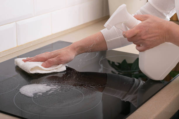 Woman cleans ceramic stove with detergent. Cleanliness order in house, daily chores of housewives A woman cleans a ceramic stove with detergent. Cleanliness and order in the house, daily chores of housewives. Cleaning company services cropped pants photos stock pictures, royalty-free photos & images