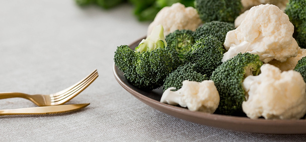 Fresh green broccoli and cauliflower on a plate on a linen tablecloth. Broccoli cabbage leaves. Light background. Vegetarian food. Healthy lifestyle.
