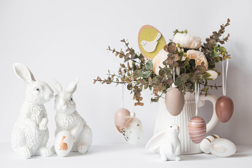 A beautiful postcard. Banner. The concept of a bright Easter holiday. Bouquet of flowers, white rabbits and Easter eggs on a white isolated background.