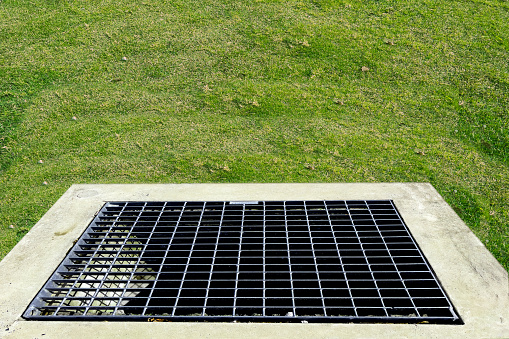 Metal grate of water drain in grass garden field. Steel rusty grating in the grass garden and concrete background.