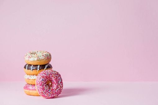 Delicious dessert. Pink, white and chocolate donuts with multicolored sprinkles on a pink background of Sweets. Confectionery products.