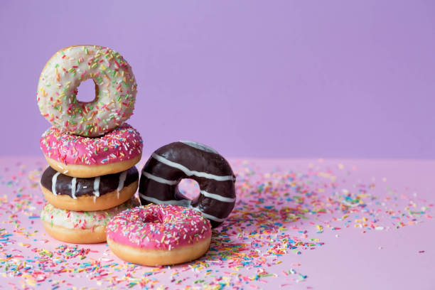 istock Delicious dessert. Pink, chocolate and white donuts with multicolored sprinkles on a purple background of Sweets. Confectionery products. 1467576532