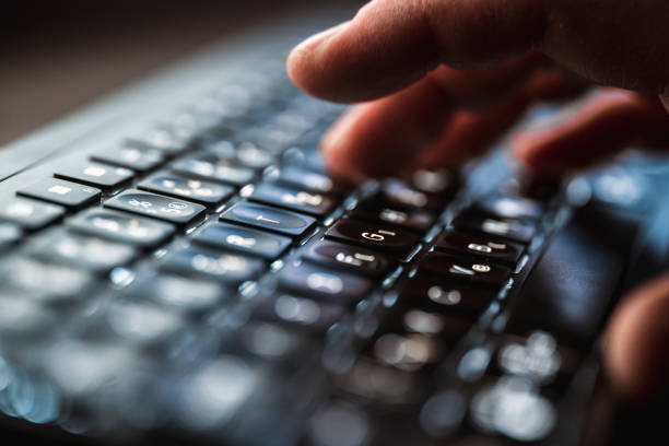 Close up shot of finger tapping a black computer keyboard during night time. Keyboard has an inner light coming under it.